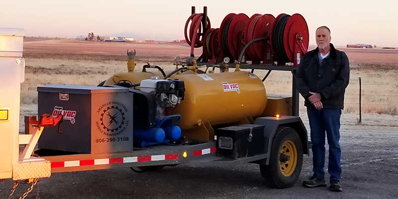 Alex Hochstein standing with his Sage Oil Vac trailer in front of a field